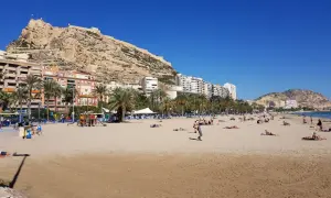 Alicante pogoda w kwietniu: słoneczna plaża z ludźmi odpoczywającymi pod zamkiem Santa Barbara.