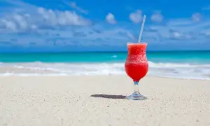 Czerwony drink na plaży, idealny do nauki słówek po hiszpańsku. Błękitne morze i piasek tworzą rajski krajobraz.