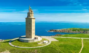 Wieża Herkulesa, najstarsza działająca latarnia morska, dumnie stoi nad błękitnym oceanem, otoczona zielonymi wzgórzami.