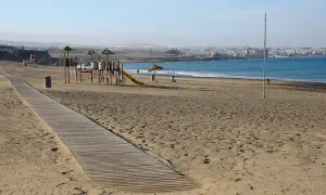 Plaża w stolicy Fuerteventury, z placem zabaw i drewnianą ścieżką. W tle widać ocean i zabudowania miasta.