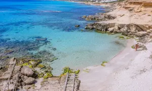 Rajska plaża Ses Illetes z turkusową wodą i piaszczystym brzegiem, gdzie para spaceruje brzegiem morza.