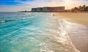 Piękne, turkusowe morze obmywa piaszczyste wybrzeże Costa Blanca. W oddali widać hotel i palmy.