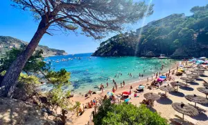 Słoneczne plaże w Hiszpanii tętnią życiem. Ludzie kąpią się w turkusowej wodzie, opalają na piasku pod parasolami i spacerują brzegiem morza.