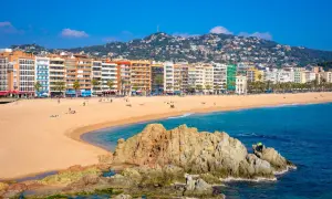 Słoneczna plaża w Lloret de Mar z kolorowymi budynkami w tle i skalistym wybrzeżem.
