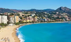Malaga plaża z turkusową wodą i zabudowaniami na wzgórzach. Słoneczny dzień nad Morzem Śródziemnym.
