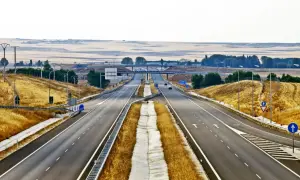Pusta autostrada w Hiszpanii, z suchą trawą po bokach i mostami w oddali.