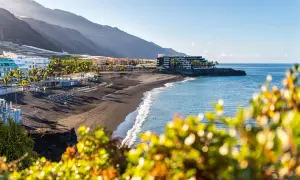 Słoneczne la palma plaże z czarnym piaskiem, palmami i hotelami w tle. Błękitne morze łagodnie faluje.