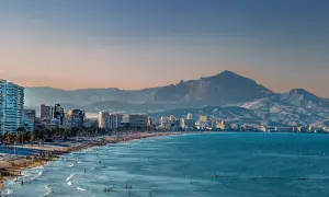Alicante pogoda w grudniu: słoneczna plaża z ludźmi, turkusowe morze i góry w tle.