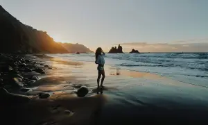 Zachód słońca na plaży, idealna pogoda na Wyspach Kanaryjskich w październiku. Kobieta podziwia fale i skaliste wybrzeże.