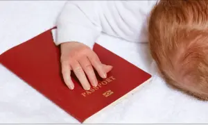 Dziecko z rudymi włosami śpi na białym ręczniku, jego dłoń spoczywa na czerwonym paszporcie. Czy do Hiszpanii trzeba paszport?