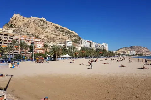 Alicante pogoda w kwietniu: słoneczna plaża z ludźmi odpoczywającymi pod zamkiem Santa Barbara.