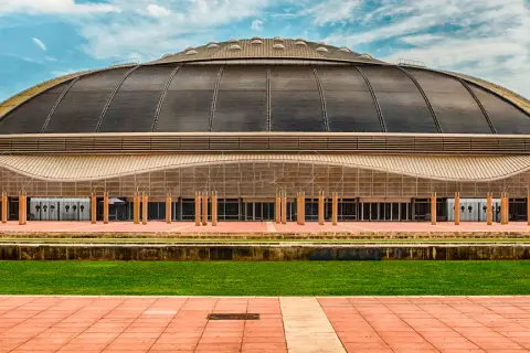 Palau Sant Jordi, z charakterystyczną kopułą, prezentuje się imponująco na tle błękitnego nieba z chmurami.