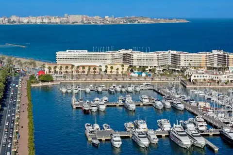 Alicante wczasy: luksusowe jachty w marinie, hotel Meliá Alicante i plaża z palmami.