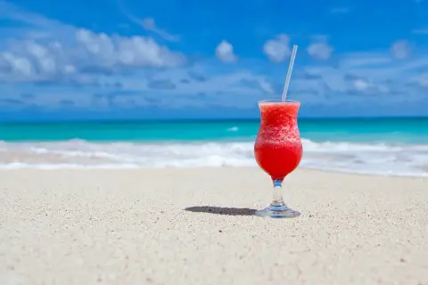 Czerwony drink na plaży, idealny do nauki słówek po hiszpańsku. Błękitne morze i piasek tworzą rajski krajobraz.