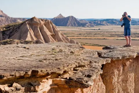 Mężczyzna robi zdjęcie na krawędzi klifu w Bardenas Reales, podziwiając surowy, pustynny krajobraz.