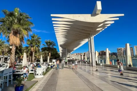 Spacerem po malaga park, pod palmami i nowoczesną pergolą, ludzie odpoczywają w kawiarniach i spacerują.