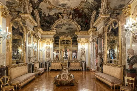 Złocone wnętrze pałacowe, przypominające salę w madryckich muzeach, z malowidłami na suficie i bogatymi meblami.