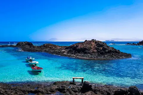 Fuerteventura w lutym: spokojne, turkusowe morze, skaliste wybrzeże i łodzie kołyszące się na falach. Idealna pogoda na relaks.