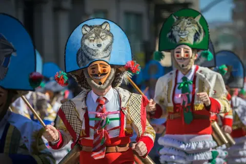 Ludzie w maskach i barwnych strojach, święta w Hiszpanii. Widać malunek wilka na kapeluszu.