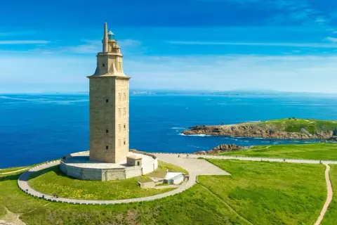 Wieża Herkulesa, najstarsza działająca latarnia morska, dumnie stoi nad błękitnym oceanem, otoczona zielonymi wzgórzami.