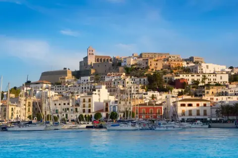 Widok na port z żaglówkami i wzgórzem z białymi domami i katedrą. Ibiza atrakcje zachwycają!