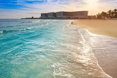 Piękne, turkusowe morze obmywa piaszczyste wybrzeże Costa Blanca. W oddali widać hotel i palmy.