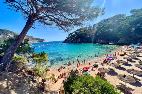 Słoneczne plaże w Hiszpanii tętnią życiem. Ludzie kąpią się w turkusowej wodzie, opalają na piasku pod parasolami i spacerują brzegiem morza.