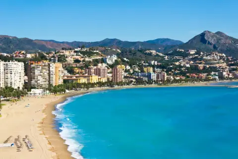 Malaga plaża z turkusową wodą i zabudowaniami na wzgórzach. Słoneczny dzień nad Morzem Śródziemnym.