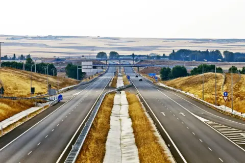 Pusta autostrada w Hiszpanii, z suchą trawą po bokach i mostami w oddali.