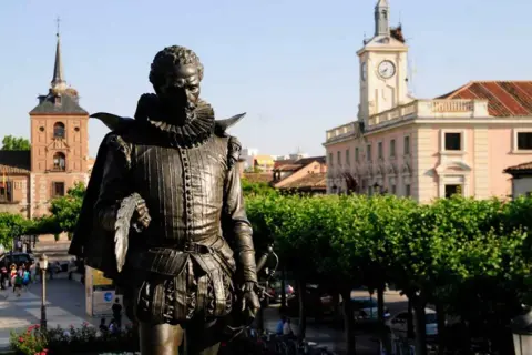 Pomnik Cervantesa w Alcalá de Henares, z ratuszem i wieżą zegarową w tle.