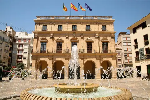 Fontanna na placu przed ratuszem w Castellón de la Plana, Walencja. Flagi Hiszpanii i regionu Walencji powiewają na dachu.