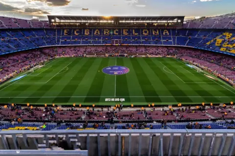 Widok na pusty stadion FC Barcelona, Camp Nou, z rzędem siedzeń w kolorach klubu i zieloną murawą.