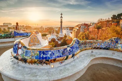 Kolorowa mozaika zdobi ławkę w Parku Güell, dziele Gaudiego. W tle widać panoramę Barcelony o zachodzie słońca.