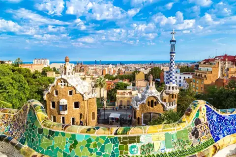Kolorowe budowle Antonio Gaudiego w Parku Güell, Barcelona, z widokiem na miasto i morze.