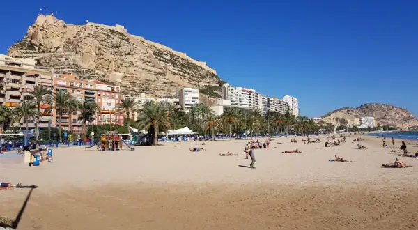 Alicante pogoda w kwietniu: słoneczna plaża z ludźmi odpoczywającymi pod zamkiem Santa Barbara.