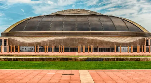 Palau Sant Jordi, z charakterystyczną kopułą, prezentuje się imponująco na tle błękitnego nieba z chmurami.