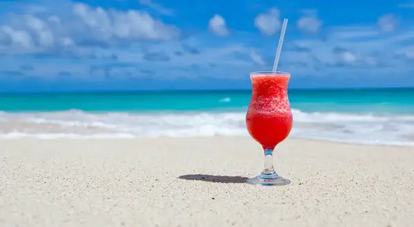 Czerwony drink na plaży, idealny do nauki słówek po hiszpańsku. Błękitne morze i piasek tworzą rajski krajobraz.