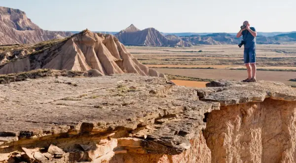 Mężczyzna robi zdjęcie na krawędzi klifu w Bardenas Reales, podziwiając surowy, pustynny krajobraz.
