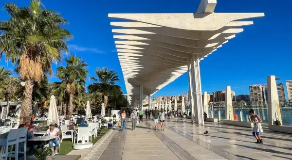 Spacerem po malaga park, pod palmami i nowoczesną pergolą, ludzie odpoczywają w kawiarniach i spacerują.