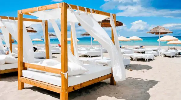 Luksusowe noclegi Hiszpania: białe baldachimy i leżaki na piaszczystej plaży, turkusowe morze i błękitne niebo.