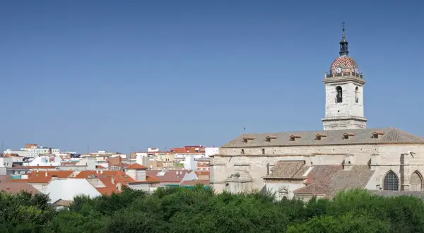 Widok na miasto Ciudad Real z kościołem i jego wieżą zegarową na tle błękitnego nieba.