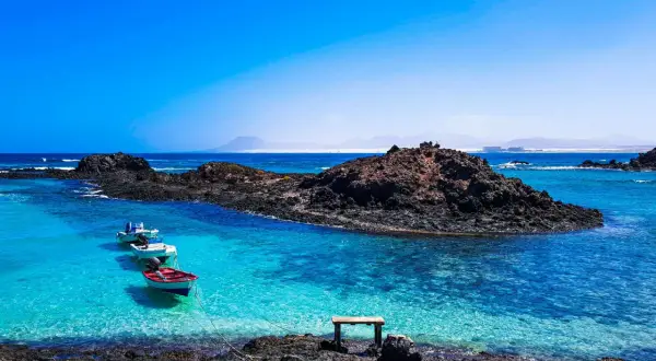 Fuerteventura w lutym: spokojne, turkusowe morze, skaliste wybrzeże i łodzie kołyszące się na falach. Idealna pogoda na relaks.
