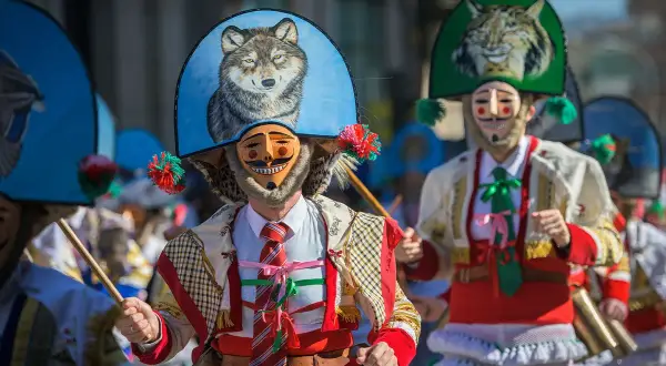 Ludzie w maskach i barwnych strojach, święta w Hiszpanii. Widać malunek wilka na kapeluszu.