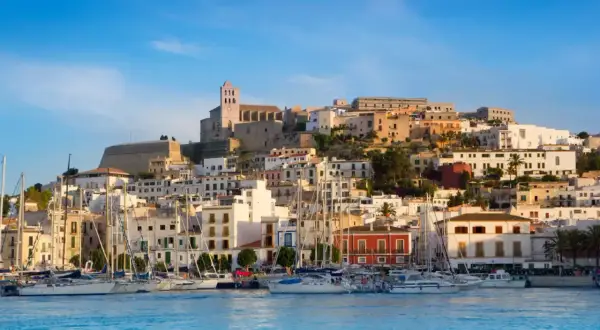 Widok na port z żaglówkami i wzgórzem z białymi domami i katedrą. Ibiza atrakcje zachwycają!