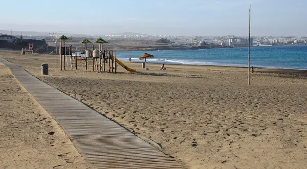 Plaża w stolicy Fuerteventury, z placem zabaw i drewnianą ścieżką. W tle widać ocean i zabudowania miasta.