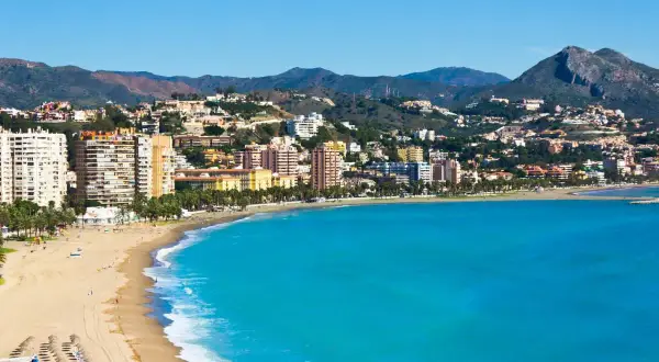 Malaga plaża z turkusową wodą i zabudowaniami na wzgórzach. Słoneczny dzień nad Morzem Śródziemnym.