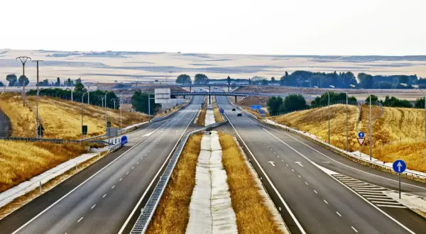 Pusta autostrada w Hiszpanii, z suchą trawą po bokach i mostami w oddali.