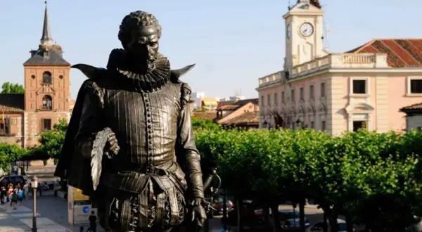 Pomnik Cervantesa w Alcalá de Henares, z ratuszem i wieżą zegarową w tle.