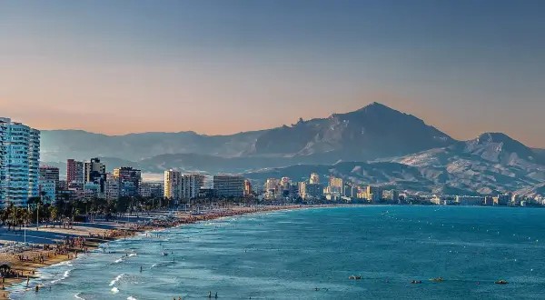 Alicante pogoda w grudniu: słoneczna plaża z ludźmi, turkusowe morze i góry w tle.