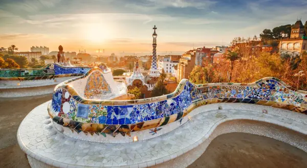 Kolorowa mozaika zdobi ławkę w Parku Güell, dziele Gaudiego. W tle widać panoramę Barcelony o zachodzie słońca.